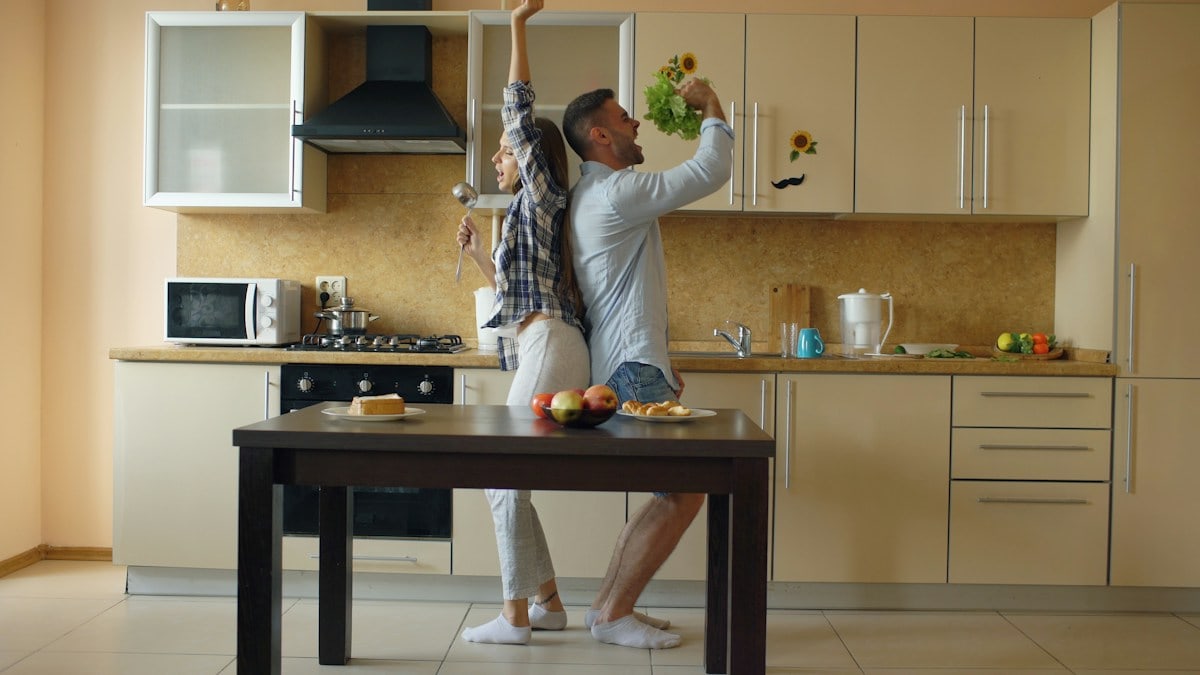 Attractive young joyful couple have fun dancing and singing while cooking in the kitchen at home in the morining